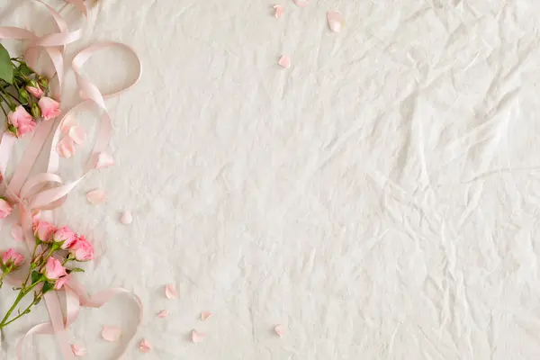 Açık pembe güllerin ve beyaz keten arka planda kopyalanmış kurdeleli taç yapraklarının üst görüntüsü. Yıldönümü, düğün ya da anneler günü için pankart tasarımı