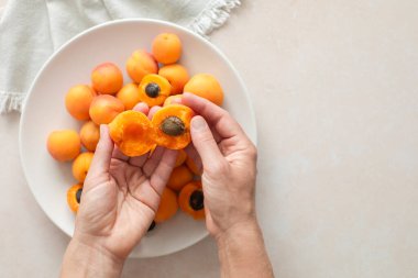 Bir kadının iki eli yukarıda, yarım kayısı tutan, taze olgun kayısılarla dolu bir tabağın üzerinde, fotokopi alanı olan.