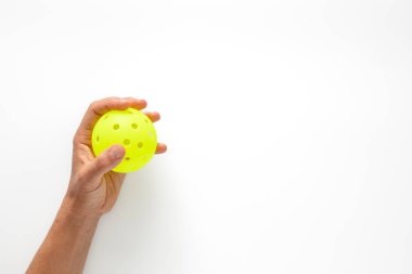 Fotokopi alanı olan beyaz zemin üzerinde parlak sarı bir picleball tutan elin yakın görüntüsü. Pickleball etkinliği için pankart