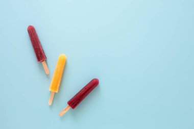 Açık mavi arkaplan üzerinde sarı ve kırmızı renkte üç buzlu dondurmanın üst aşağı görünümü