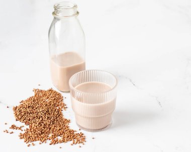 Karabuğday sütü ve kavrulmuş karabuğday tanelerini beyaz mermer masa üstünde fotokopi alanı olan temiz bir bardak ve şişenin yakın görüntüsü