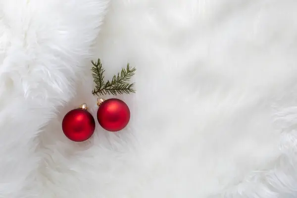 Küçük bir çam dallı, sahte beyaz kürk arka planda iki kırmızı Noel süsü.
