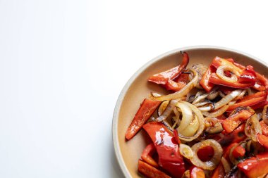 Beyaz zemin üzerinde Shakshuka Bell biberleri ve soğanları olan sarı seramik bir tabağın yakın çekim görüntüsü.