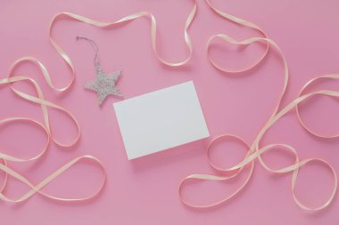 Pembe arka planda, kurdeleli ve gümüş yıldız süslemeli beyaz kart.