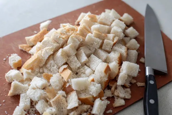 Kahverengi kesme tahtasının üzerinde kesilen ekmeğin kenarındaki bıçakla yakın görüntüsü.