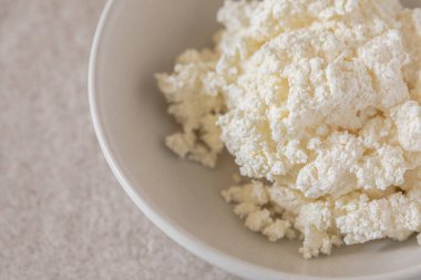 Tezgahın üzerine seramik bir tabakta taze çiftçi peynirinin yakın plan görüntüsü. Doğal tasarım, sağlıklı yemek, süt ve zanaatkar gıda kavramları için idealdir..