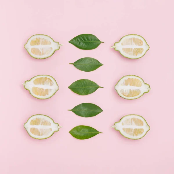 将新鲜的有机柠檬和绿叶整齐地摆放在粉红的背景上 最小平铺 — 图库照片