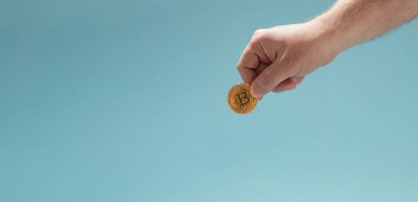 Bir adamın eli açık mavi arka planda altın bir Bitcoin para tutuyor. Boşluğu kopyala.