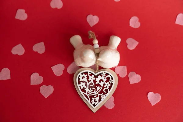 Two white birds in love on a red background with pink hearts around and a big wooden heart.