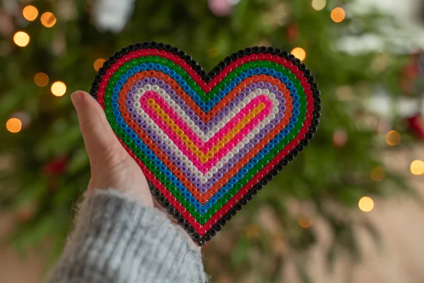 Rainbow heart in a hand on the background of a Christmas tree with lights and bokeh.