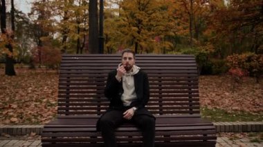 Adamın biri parkta elektronik sigara içiyor. Bankta oturuyor. Baharda.