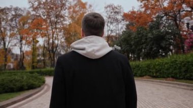 Bir adam parkta yürüyor, arkadan bakıyor.