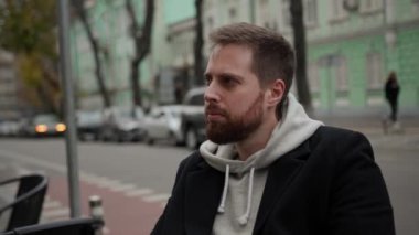 Paltolu genç bir adam caddedeki kafede oturuyor ve birini bekliyor.