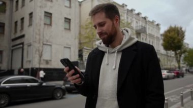 Şehirde ceketli çekici bir adam telefonla konuşuyor ve gülümsüyor.