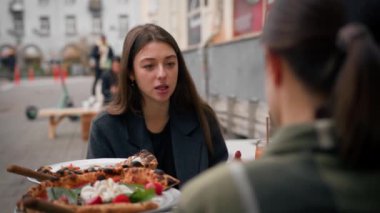 İki arkadaş terasta bir restoranda tanışmışlar. Pizza yiyip kokteyl içiyorlar.