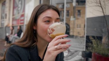 Bir kız restoranın terasında tek başına oturur ve kokteyl içer.