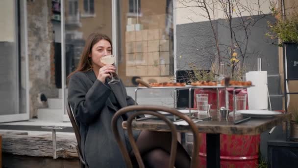 一个女孩一个人坐在餐馆的阳台上喝鸡尾酒 — 图库视频影像