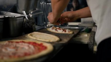 Profesyonel şef geleneksel pizza yapar. Şef küçük bir pizzaya malzeme ekler.