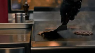 Restoranın mutfağındaki şef hamburgerler için pirzola yapar. Biftek ezer.