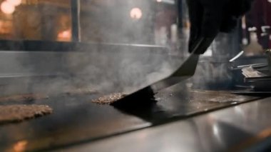 Restoranın mutfağındaki şef hamburgerler için pirzola yapar. Biftek ezer.