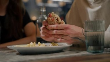 Yakın plan. Bir adam, arkadaşlarıyla birlikte hamburger ve patates kızartması yiyor.