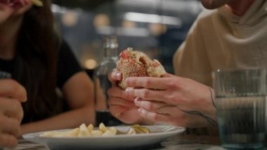 Yakın plan. Bir adam, arkadaşlarıyla birlikte hamburger ve patates kızartması yiyor.