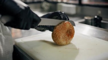 Bir restoranın profesyonel mutfağında aşçı. Hamburger ekmeği kesiyor.