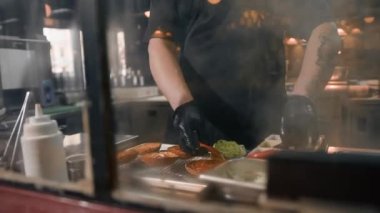 Hamburger pişirme süreci, aşçı restoran mutfağında çöreğe malzeme ekliyor.