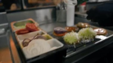 Hamburger pişirme süreci, aşçı restoran mutfağında çöreğe malzeme ekliyor.