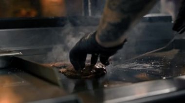 Restoranın mutfağındaki şef hamburgerler için pirzola yapar. Biftek ezer.