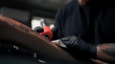 Yakın plan, bir kadının bacağına dövme yapma süreci. Erkek dövme sanatçısı dövme yapıyor.