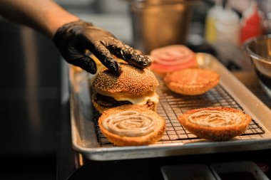 Hamburger pişirme süreci, aşçı restoran mutfağında çöreğe malzeme ekliyor.