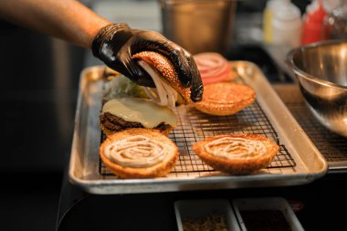 Hamburger pişirme süreci, aşçı restoran mutfağında çöreğe malzeme ekliyor.