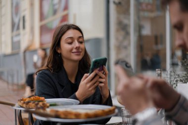 Restoranda oturmak, akıllı telefonlardan mesaj atmak. Erkek arkadaş, kız arkadaş buluşmada cep telefonuna bakıyor.