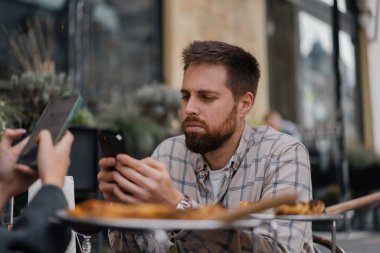 Restoranda oturmak, akıllı telefonlardan mesaj atmak. Erkek arkadaş, kız arkadaş buluşmada cep telefonuna bakıyor.