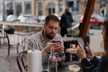 Restoranda oturmak, akıllı telefonlardan mesaj atmak. Erkek arkadaş, kız arkadaş buluşmada cep telefonuna bakıyor.