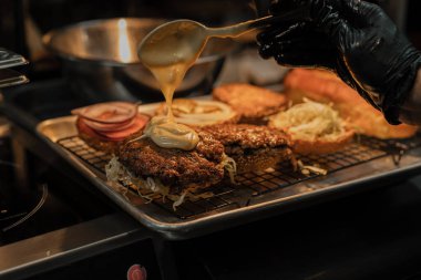 Hamburger pişirme süreci, aşçı restoran mutfağında çöreğe malzeme ekliyor.