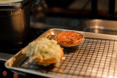 Hamburger pişirme süreci, aşçı restoran mutfağında çöreğe malzeme ekliyor.