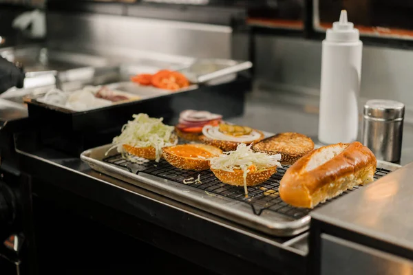 バーガーの調理法 レストランキッチンでパンに具材を加えるシェフ — ストック写真