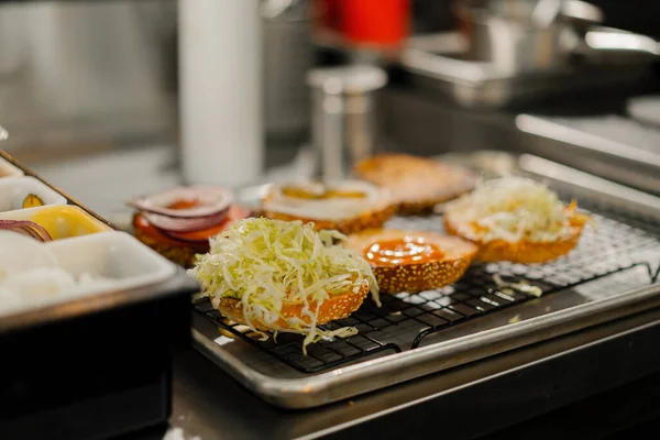 バーガーの調理法 レストランキッチンでパンに具材を加えるシェフ — ストック写真
