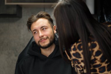 Dövme delme stüdyosu. Kadın bir erkeğe kulak delici yapar.