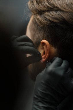 Dövme delme stüdyosu. Kadın bir erkeğe kulak delici yapar.