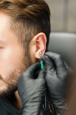 Dövme delme stüdyosu. Kadın bir erkeğe kulak delici yapar.