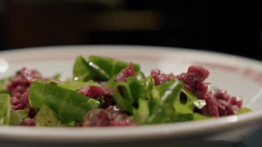 Yakın plan - Bir restoranda dönen bir masada sığır eti tartar, arka planda bulanık çalışan bir restoran