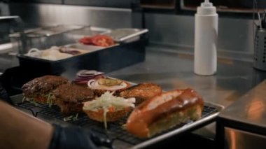 Hamburger pişirme süreci, aşçı restoran mutfağında çöreğe malzeme ekliyor.
