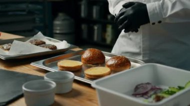 Profesyonel mutfak: şef hamburgeri malzemeler ekleyerek hazırlar