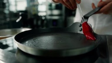 Profesyonel mutfak: Aşçı, profesyonel sobanın tepsisine yağ sürüyor..