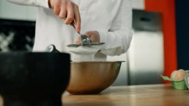 Erkek şef, profesyonel bir mutfakta kaşıkla yemek kâsesine un süzüyor. Restoranda para kazanıyordum.