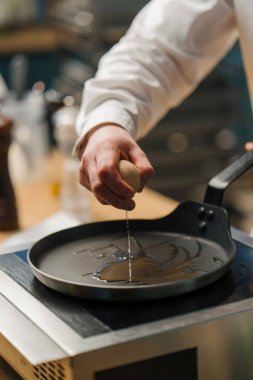 Bir aşçı, profesyonel mutfakta kahvaltı hazırlarken bir yumurtayı tavaya kırar.