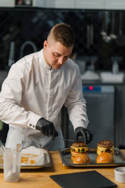 Şef leziz bir hamburger hazırlıyor. Profesyonel mutfak burgeri, etli peynirli, domatesli, kızarmış salatalı.